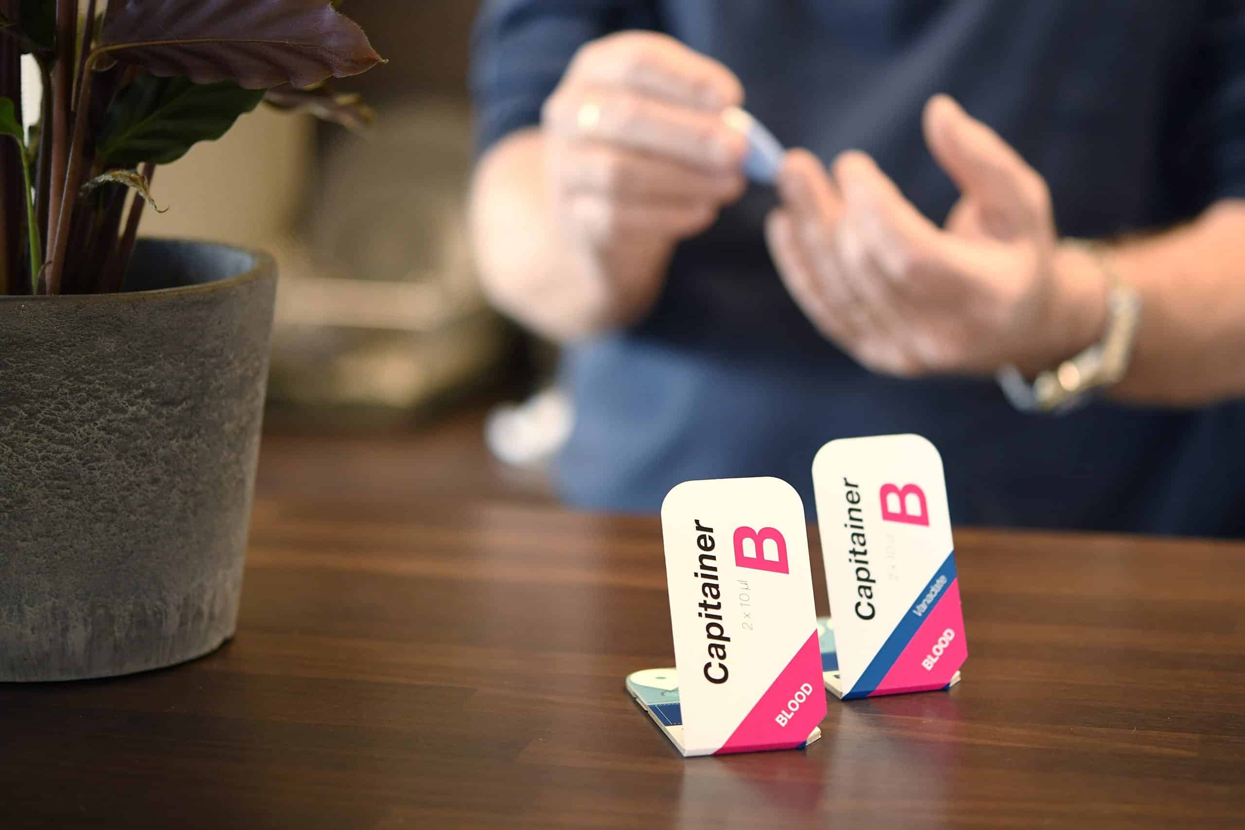 Two Capitainer blood sampling cards and a man with a lancet.